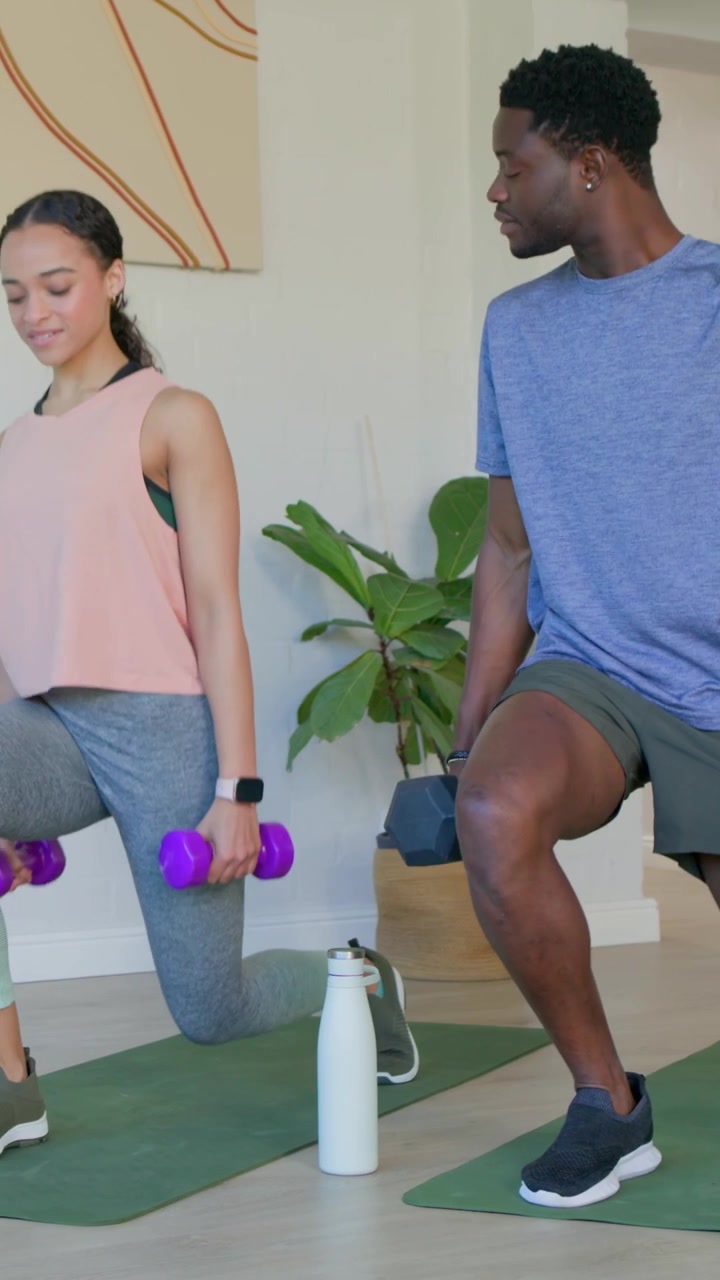 Vertikal video: Mand skifter position, laver omvendte lunges på hjemmemåtte i blå T-shirt med vægte til fitness.