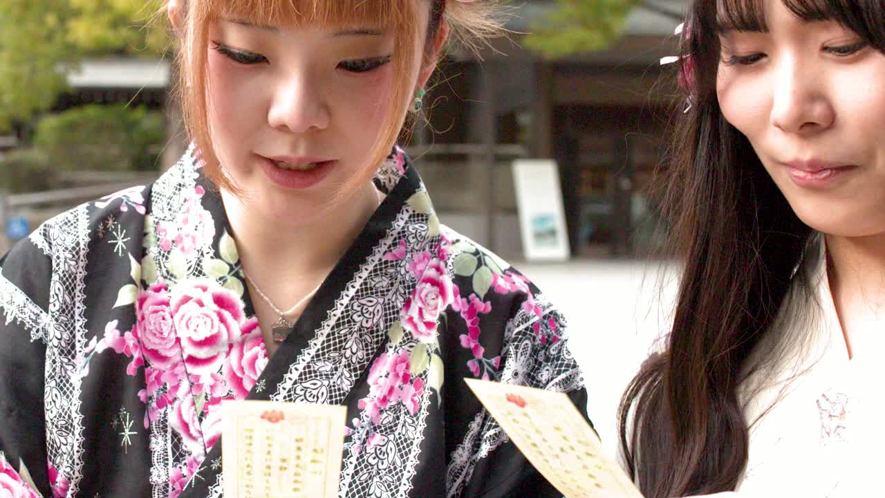 Tokyo'da bir Japon tapınağında geleneksel kimono giymiş iki kadın açık havada kağıt falı okuyor.