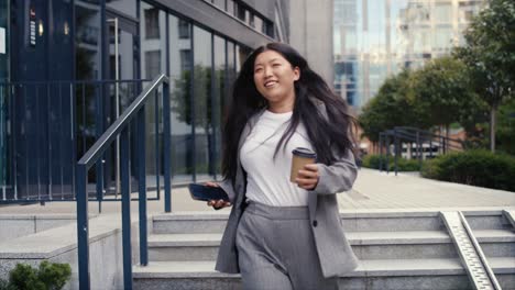 business chinese woman walking down the stairs with phone and cup of coffee