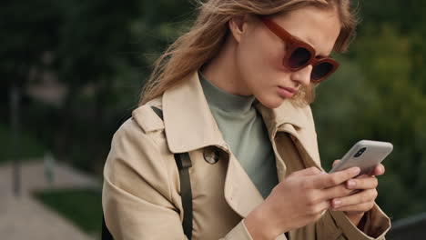 caucasian female student using smartphone and smiling outdoors.