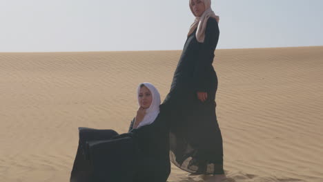 due donne musulmane che indossano abiti tradizionali e hijab in posa in un deserto ventoso 1