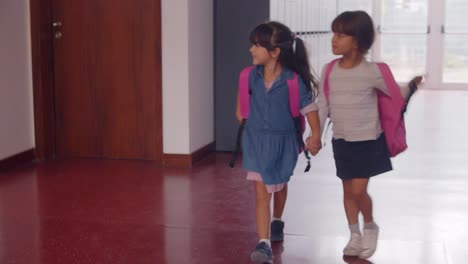 lindas y felices alumnas de la escuela primaria con mochilas rosas y caminando por la escuela cogidas de la mano