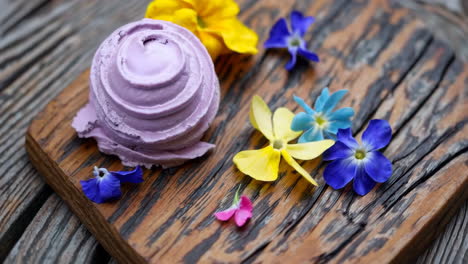 purple ice cream scoop garnished with edible flowers on a rustic wooden board