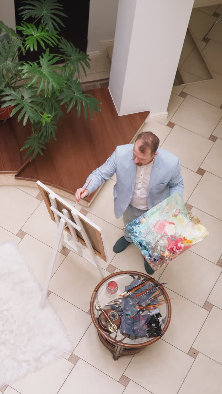 el artista traza el color en el lienzo con el pincel. el pintor maduro con una gran paleta dibuja un cuadro en el taller de arte. el hombre creativo con talento artístico en la galería