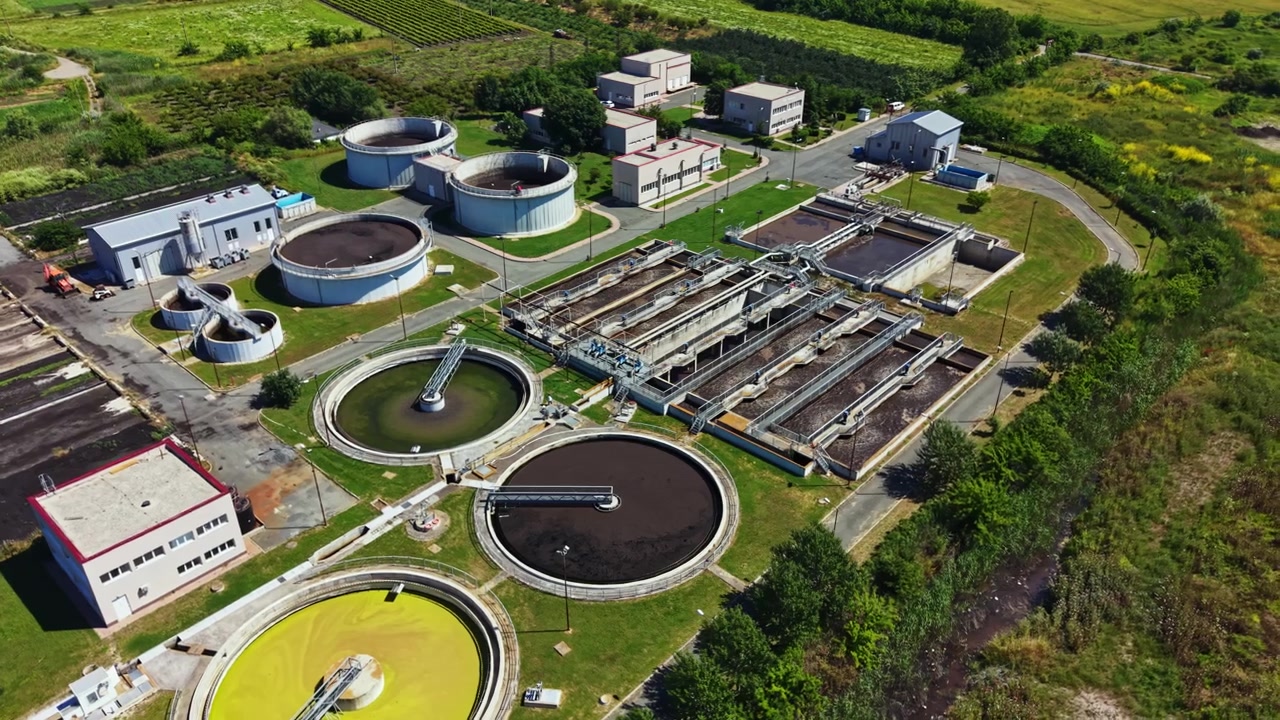Water treatment facility operates during daylight with multiple tanks, buildings, and green areas nearby