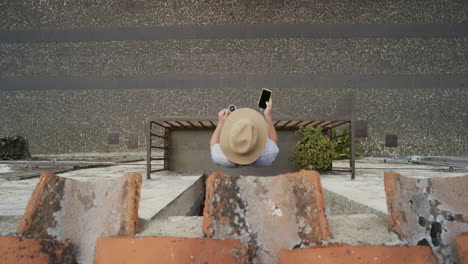 woman using smartphone drinking coffee enjoying summer vacation browsing online messages relaxing on balcony texting wearing hat above view