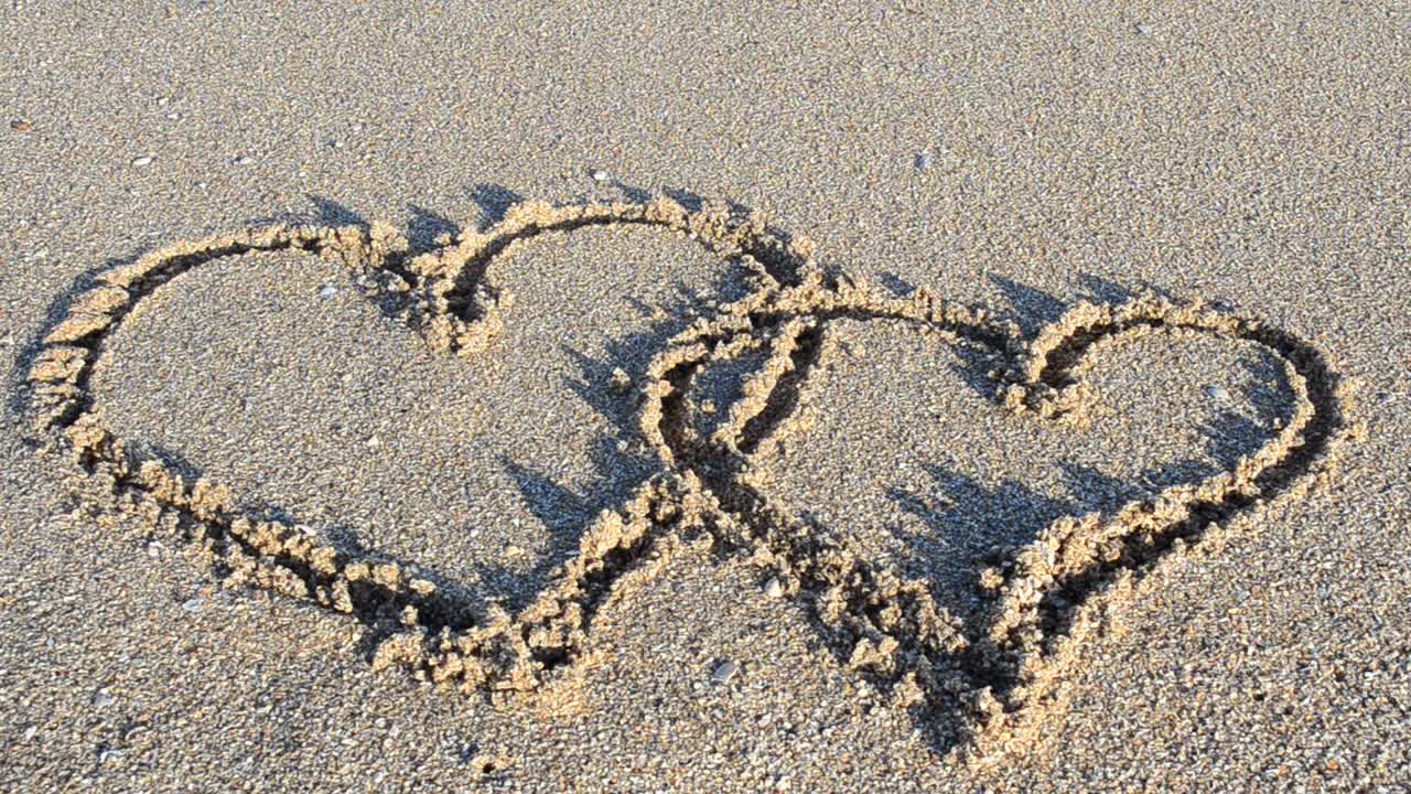 The drawing heart on sand. Heart is washed away by a sea wave. Shooting on the beach