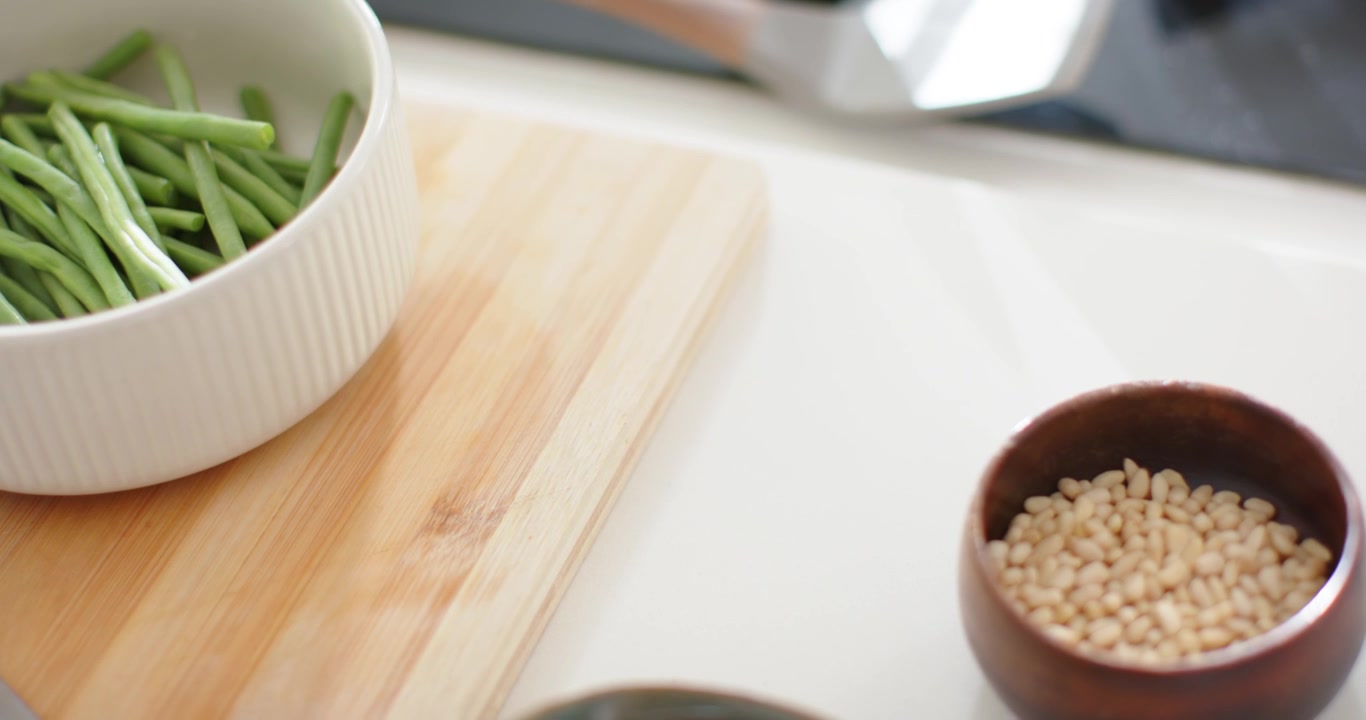 Camera panning right, white ribbed bowl of green beans on cutting board, revealing nuts and berries