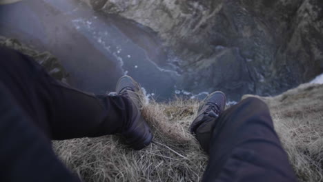 piernas de hombre sentado en el acantilado y disfrutar de la vista del pintoresco cañón en islandia