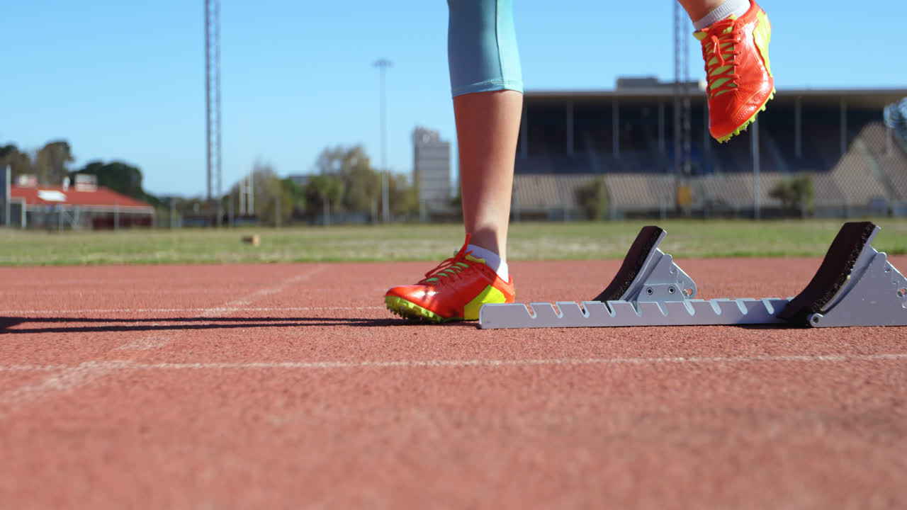 sección baja de una atleta femenina tomando la posición inicial en una pista de correr en un lugar deportivo 4k