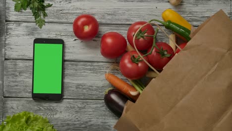 dos tomates frescos rodando cerca de las verduras y el teléfono inteligente