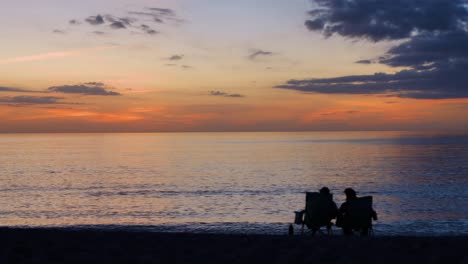 couple sitting in chairs on beach watching sunset