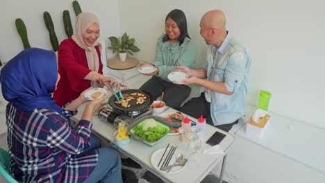 happy asian muslim mother puts slice cooked beef on family plates at a korean barbecue party at home