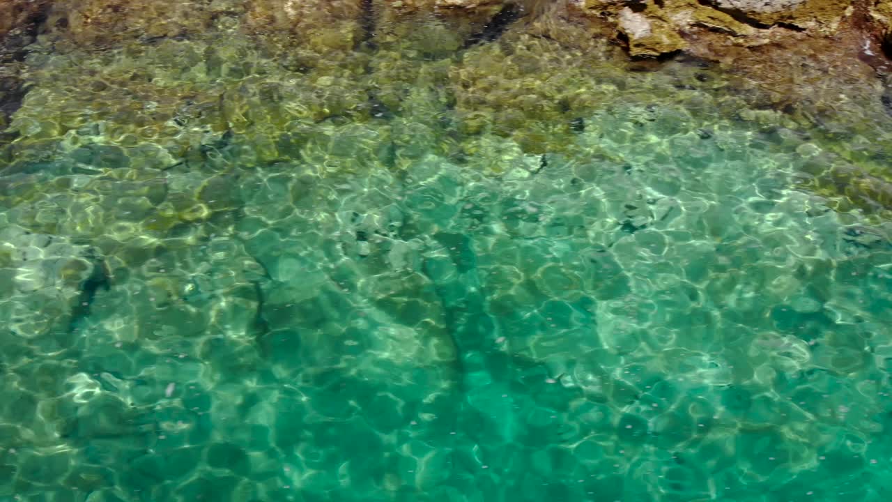 Mar cristalino esmeralda em costa rochosa, refletindo a luz do sol, textura da água para espaço de texto.