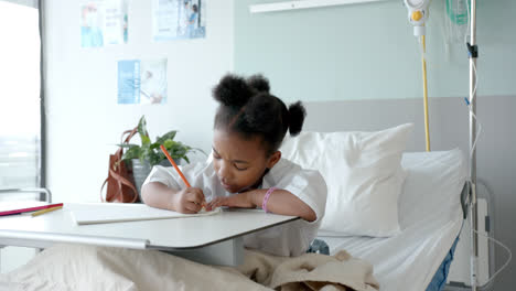 Niña-Afroamericana-Dibujando-En-Un-Cuaderno-En-La-Cama-De-Un-Hospital,-En-Cámara-Lenta