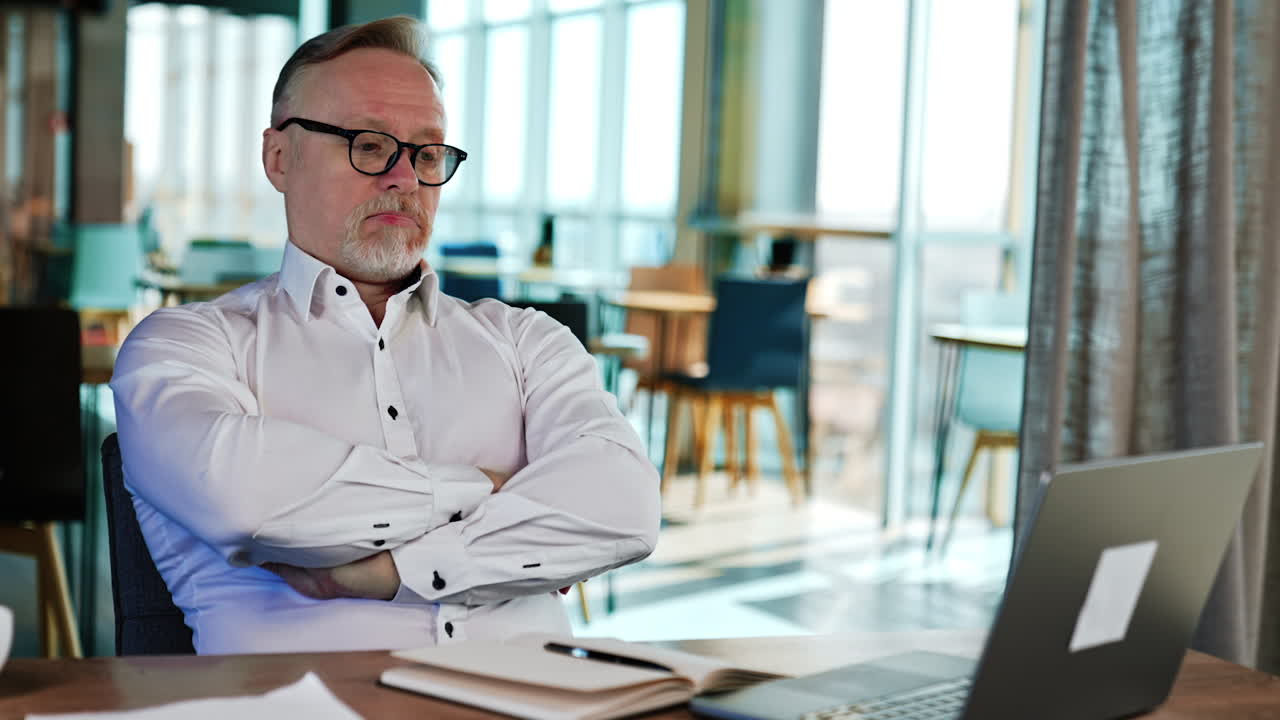 Senior bearded Caucasian businessman works on his laptop. Man looks carefully at monitor and leans back in the chair looking puzzled.