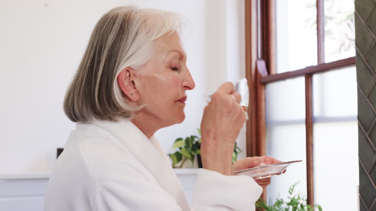 Senior woman drinking tea by window, relaxing in peaceful home environment
