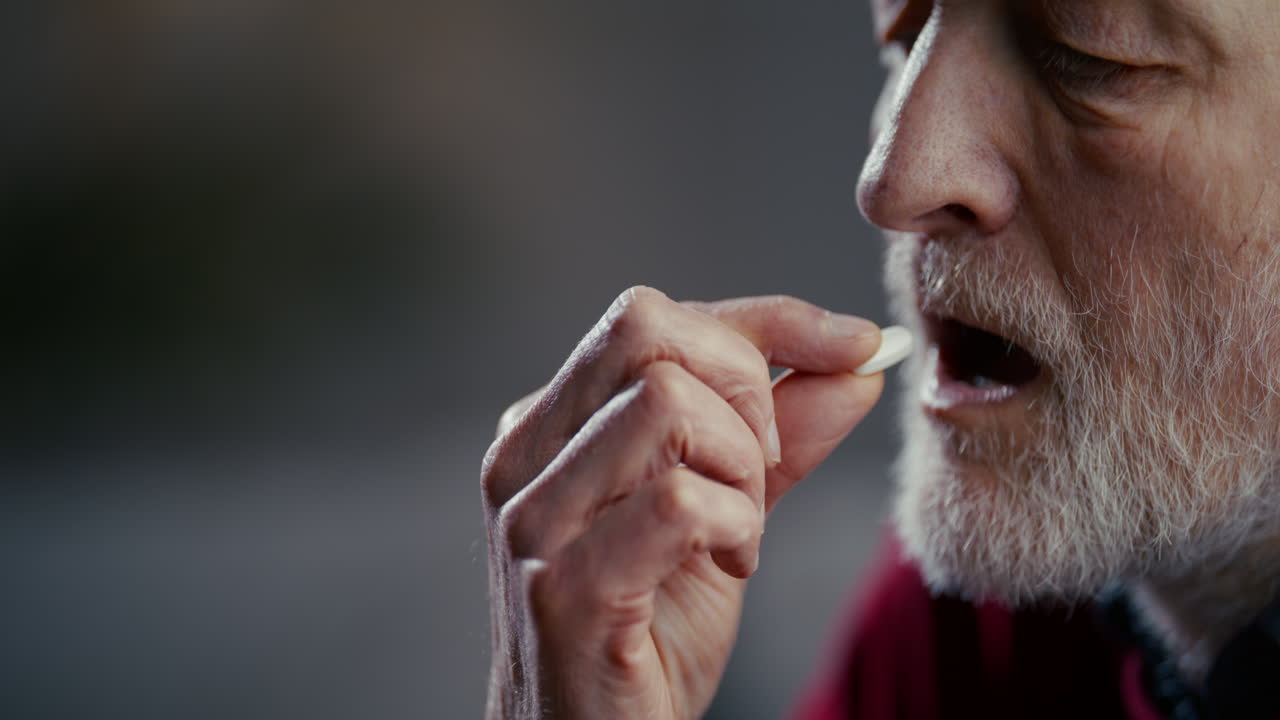 Homem Idoso Tomando uma Pílula Branca em Close-Up