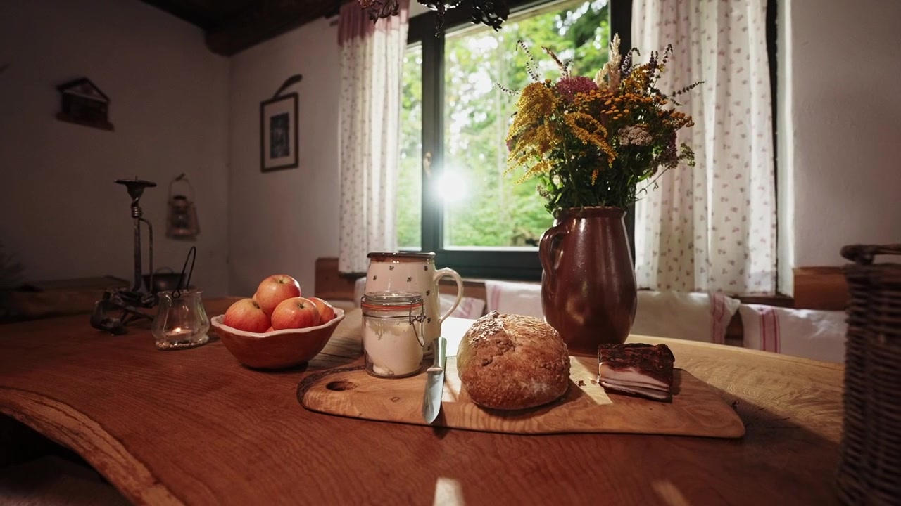 Fresh bread, pottery and a vase of flowers on a wooden table beside a sunlit window in a rustic cottage kitchen, creating a cozy atmosphere of traditional country living.