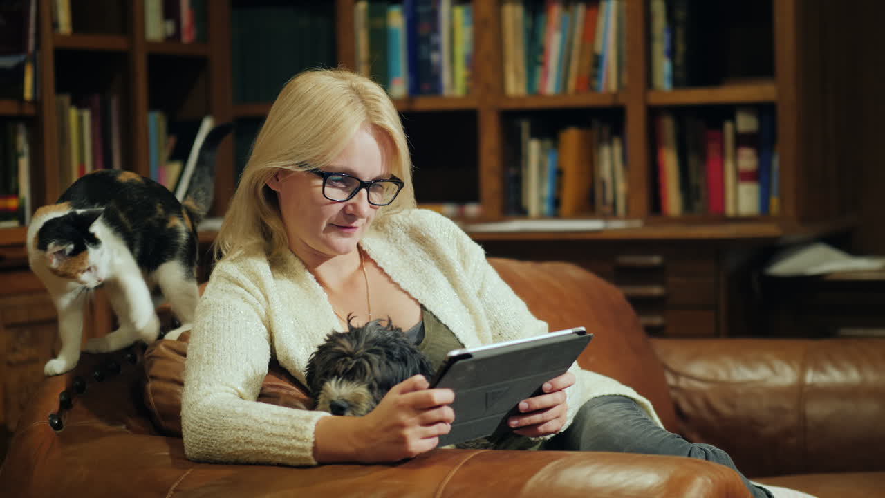 한 여성이 태블릿으로 책을 읽고 고급스러운 도서관 뒤편에 앉아 있습니다.
