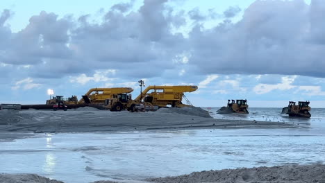 heavy machinery moving sand on a beach at sunset