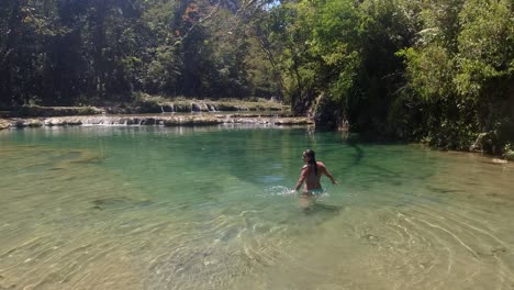 mujer latina en bikini azul camina en el río del bosque tropical verde