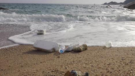 Hush-wave-washing-over-plastic-trash-on-the-beach,-Low-angle-parallel-static-4K-front-shot