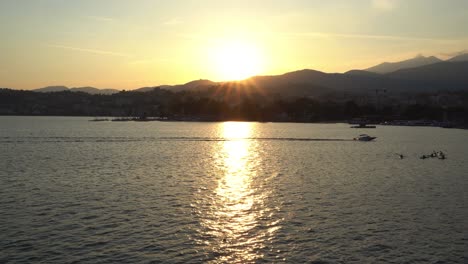 speedboat crosses lake with beautiful sunset behind, mountains surround the landscape