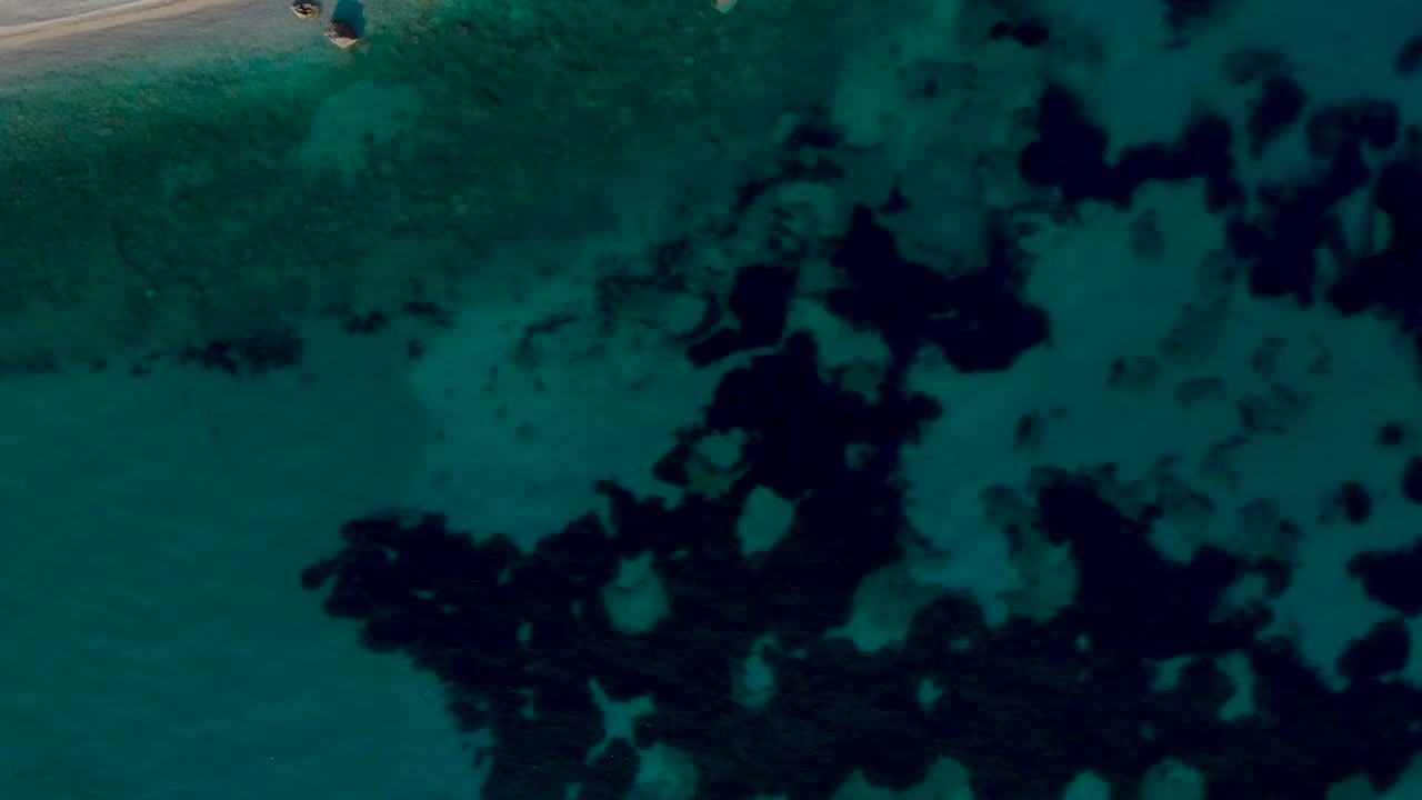 Seabed pattern under turquoise water near paradise beach with pebbles and rocks, top down view