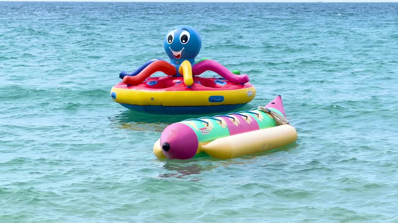 Vibrant inflatable water toys float on clear turquoise ocean water under bright natural daylight