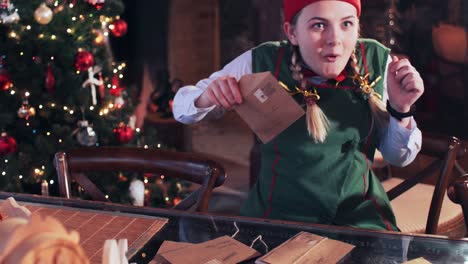 a girl in a green suit opens and looks in envelopes with letters. santa claus residence with christmas tree and fireplace