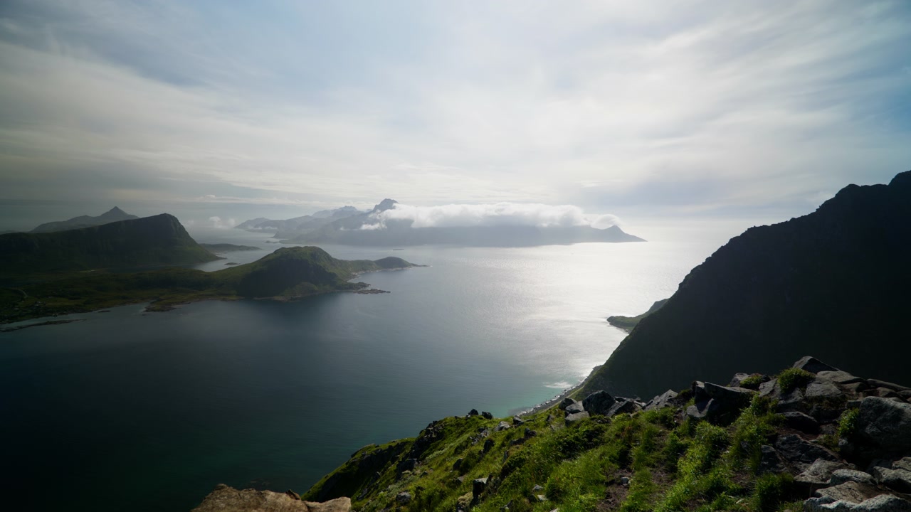 Høj kystskråning med udsigt over stille nordisk hav og spredte øer under diset sollys i Lofoten