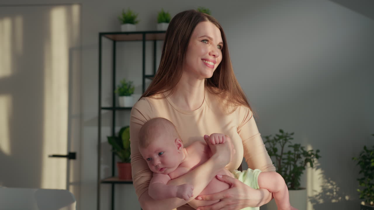 Une femme berce un nouveau-né dans ses bras, une douce lumière du soleil illumine la scène avec des ombres délicates et des plantes.
