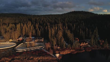 Sensational-pull-away-shot-of-a-Ranch-on-Glimpse-Lake-during-sunset,-in-a-pine-tree-forest