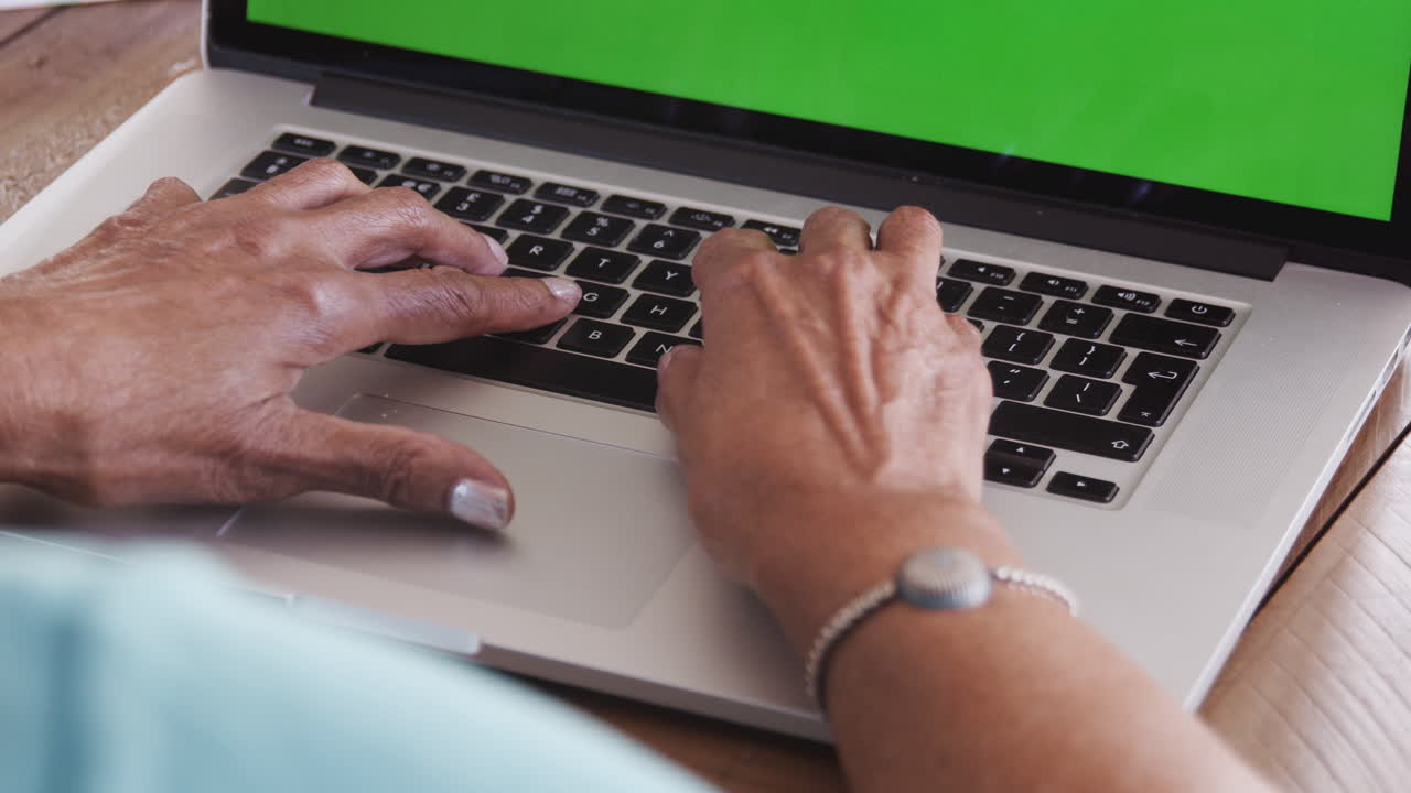 cerca de las manos de una mujer negra mayor sentada en la mesa escribiendo en un teclado de computadora portátil