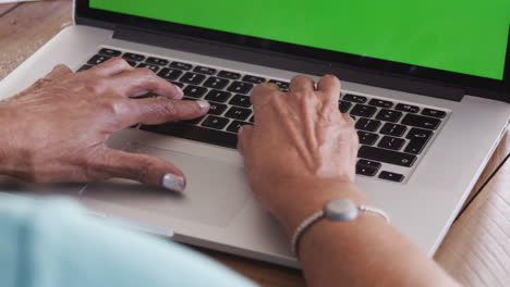 cerca de las manos de una mujer negra mayor sentada en la mesa escribiendo en un teclado de computadora portátil
