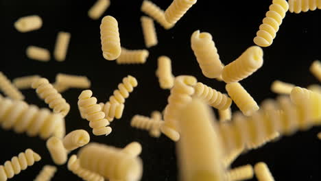 fusilli corti bucati pasta flying on the black background in slow motion and macro