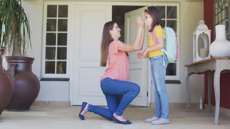 Caucasian-mother-putting-on-face-mask-and-hugging-her-daughter-outside-of-the-house