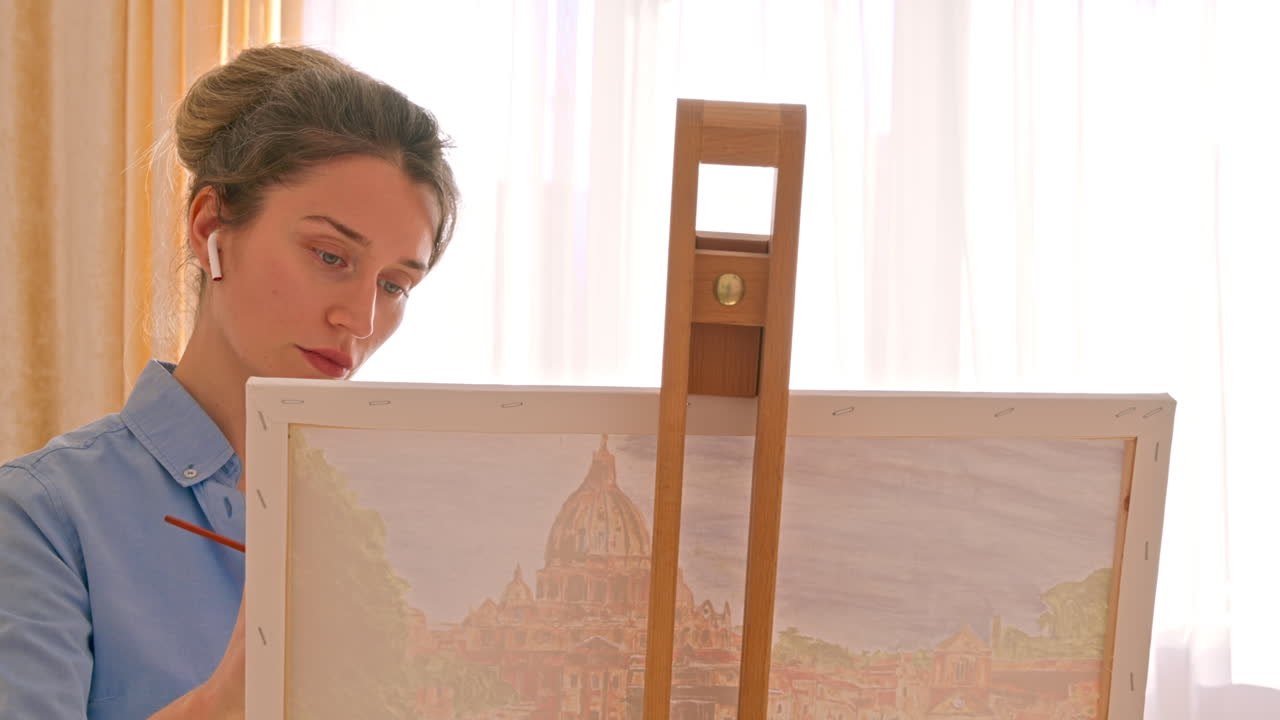 Caucasian woman painting a picture with a palette in her hands and listening music with earphones indoors