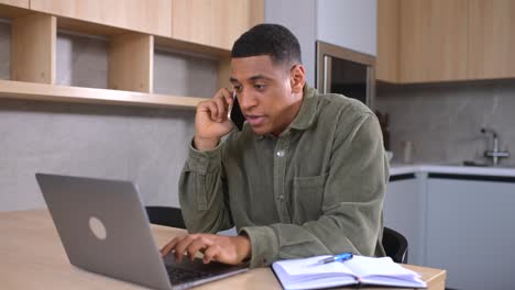 smiling multiracial guy sits at the office desk, using trendy laptop for a work