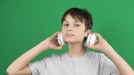 teenage boy listening to music and takes off headphones while standing in front of green screen chroma key background. portrait of kid who removes headphones from his head. 4k video