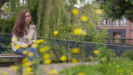 depressed woman outdoors with financial worries about cost of living crisis debt and paying bills sitting on bench in park