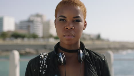 portait of independent african american woman on sunny beachfront looking serious wearing headphones