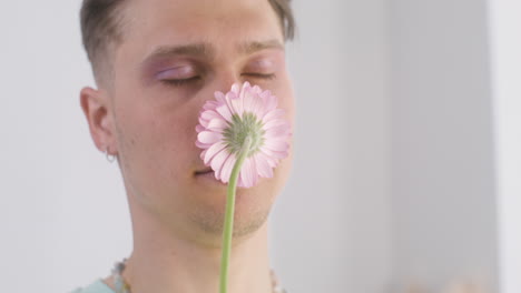 young man holding and smelling pink flower