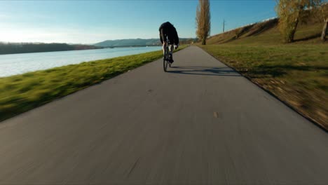 Toma-Frenética-De-Fpv-De-Carreras-De-Jake,-El-Motorista-De-Equipo-Fijo,-Junto-Al-Río-Danubio-Durante-El-Soleado-Día-De-Otoño-Tardío