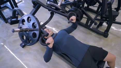 fit man in 30s exercises in chest bench press machine in health center - top down view