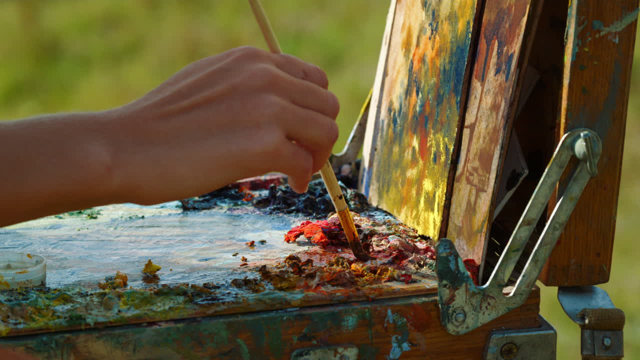artista desconocido mezclando pinturas en la paleta. dibujo a mano de primer plano en lienzo al aire libre