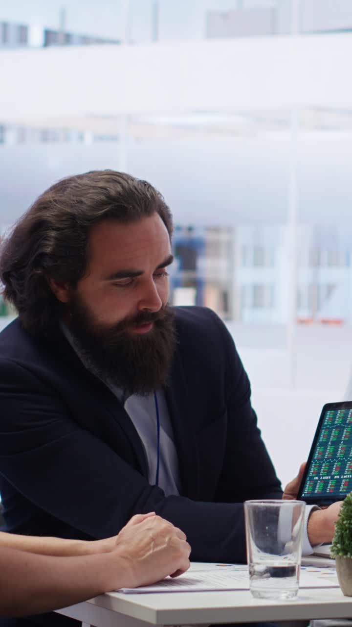 Vertikal video: Finansiel rådgiver og kunder ser på markedsandele på tablet.