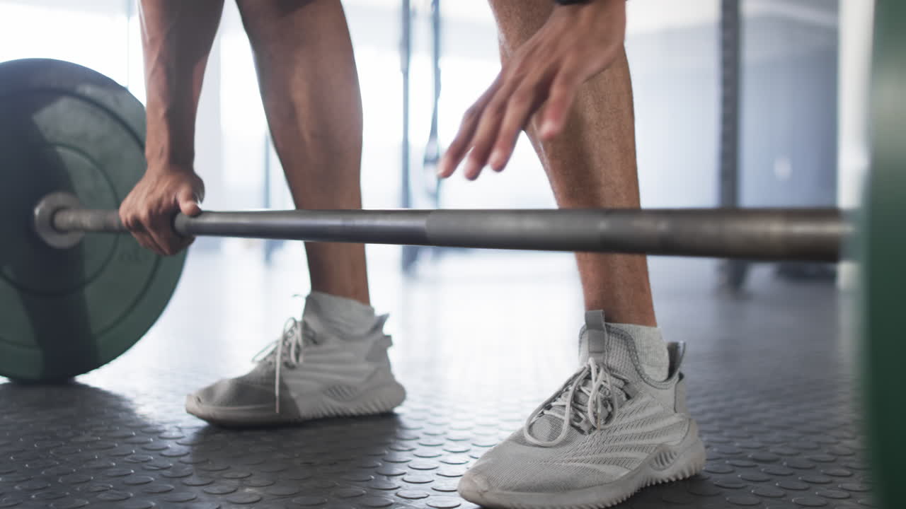Lifting barbell, man wearing smartwatch and athletic shoes in gym