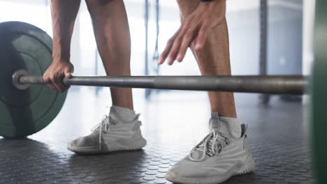 lifting barbell, man wearing smartwatch and athletic shoes in gym
